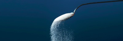 Sugar pouring out of a spoon on a blue background